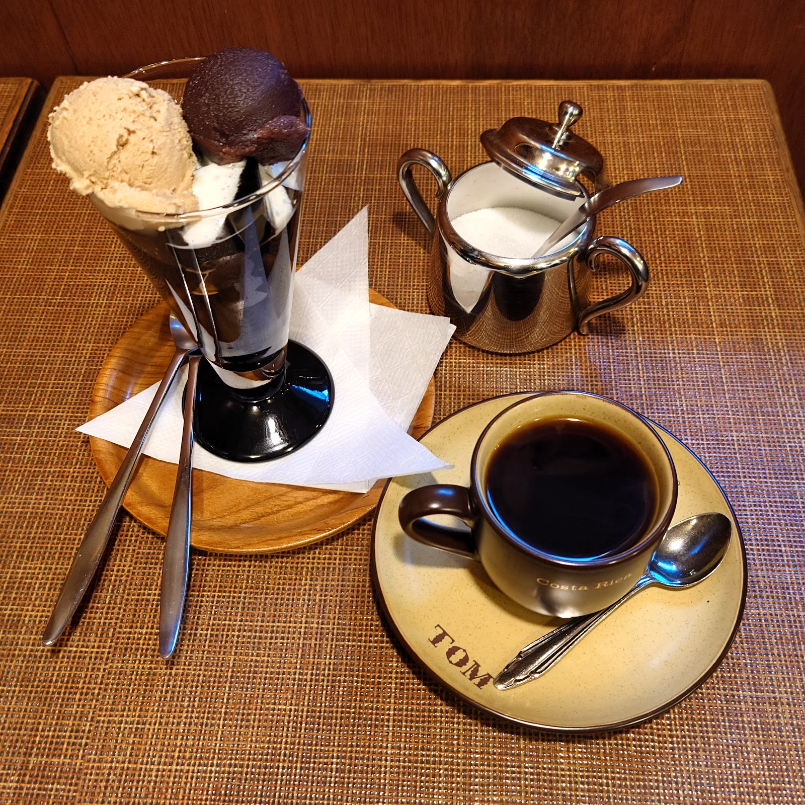 TOMロゴ入り陶器カップのブラックコーヒーと、アイスクリームと珈琲ゼリーが入ったグラスデザート、シルバーのミルクポット